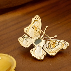 Elegant gold butterfly brooch with green gemstone and zircons on a wooden surface