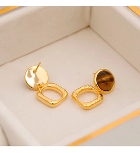 Vista macro de pendientes geométricos de ojo de tigre dorados con textura martilleada