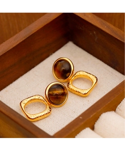 Vista macro de pendientes dorados geométricos con piedras ojo de tigre sobre madera