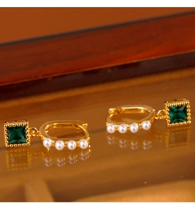 Detailed macro shot of vintage gold hoops with emerald gems and white pearls