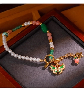 Detail eines Vintage-Perlenarmbands mit Emaille-Schmetterling und goldenem Knebelverschluss