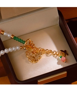 Detail eines Perlenarmbands mit goldenem Schmetterlingsanhänger auf Seidenfutter