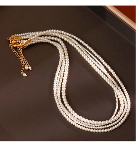 Close-up of stacked cream white 2mm pearl necklaces with gold-tone adjustable clasps