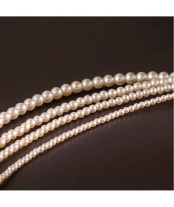 Close-up showing five different sizes of 2mm round pearl necklaces on a brown surface