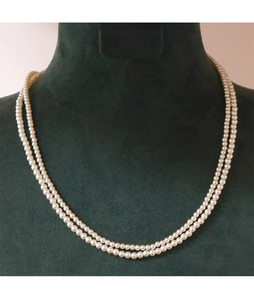 Detail of elegant double-layer 2mm white pearl necklace on dark green velvet display
