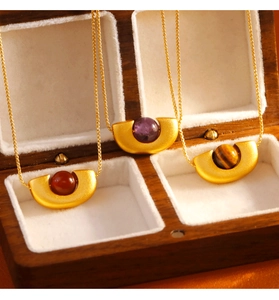 Détail de colliers dorés géométriques avec pendentifs agate rouge, améthyste et oeil de tigre