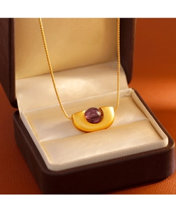 Détail d'un collier géométrique en or avec pierre violette dans un coffret cadeau