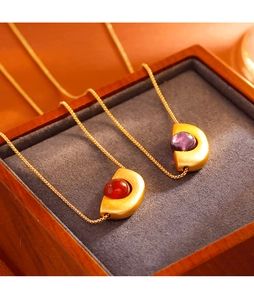 Détail de pendentifs géométriques en or avec pierres rouge et violette sur bois