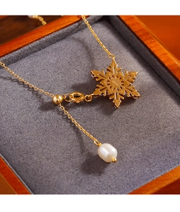 Dettaglio della collana dorata con fiocco di neve e perla su un portagioie grigio