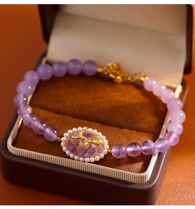 Vista macro de pulsera de cuentas de amatista con colgante de rosa dorada en caja