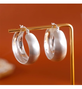 Détail de créoles en métal brossé argenté montrant la texture mate sur un support à bijoux