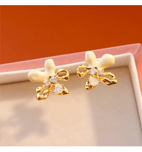 Detalle macro de pendientes de lazo de esmalte blanco con baño de oro y circonitas