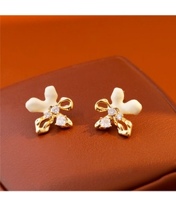 Detalle de pendientes de lazo dorado con esmalte blanco y brillantes piedras circonitas