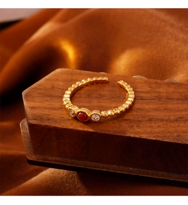 Nahaufnahme eines goldenen Perlenrings mit rotem Achat und Zirkon auf Holz und Seide