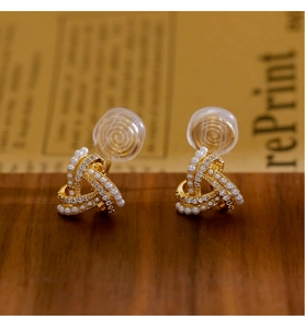 Dettaglio di orecchini a clip incrociati dorati con perle e micro diamanti su legno