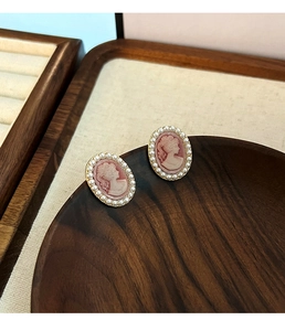 Detailed close-up of French vintage pink cameo earrings with pearls on wood
