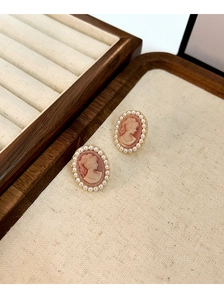 Close-up of vintage pink relief cameo earrings with faux pearl border and gold finish
