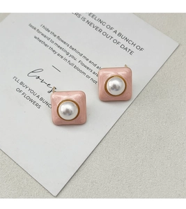 Gros plan de boucles d'oreilles carrées en émail rose avec perle et bordure dorée