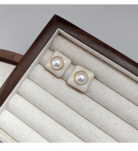 Gros plan de boucles d'oreilles carrées en perles avec bordure dorée dans un écrin