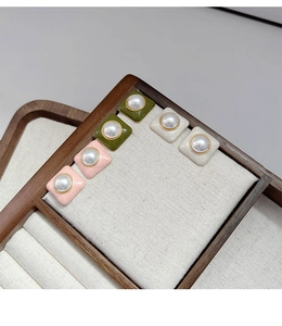 Gros plan sur des boucles d'oreilles carrées rétro en rose, vert olive et blanc crème
