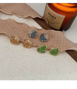 Detailed shot of square orange, blue and green crystal stud earrings on silk ribbon