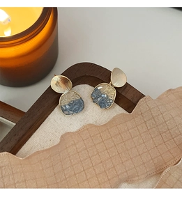 Détail de boucles d'oreilles dorées brossées avec incrustation de pierres bleues et blanches