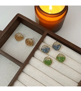 Detailed view of amber, blue, and green square stud earrings in a wooden jewelry tray