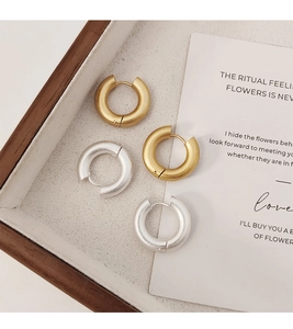 Detalle de pendientes de aro mate en oro y plata sobre una bandeja de madera mínima