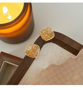 Macro detail of square amber crystal stud earrings with gold frames on a wooden tray