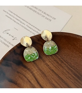 Détail de boucles d'oreilles dorées brossées avec pierres vertes sur un plateau en bois