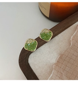 Close-up of square stud earrings with green and beige stones in a gold metal frame