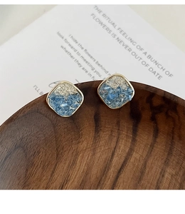 Detail of square gold earrings with blue and clear crystals on a wooden tray