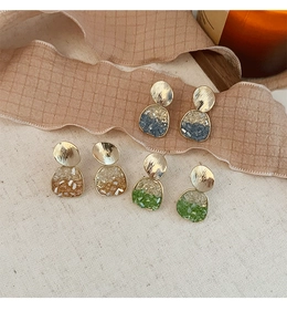 Détail de boucles d'oreilles dorées mates avec dégradés de résine sur fond textile texturé