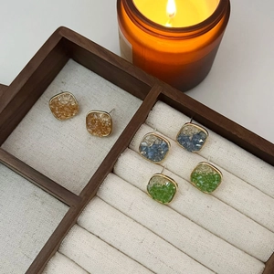 Set of three square crystal stud earrings in amber, blue, and green on a jewelry box