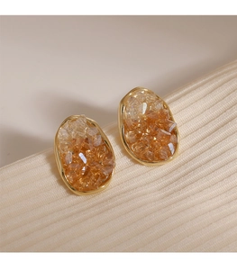 Detalle macro de pendientes de cristal ámbar con borde dorado y piedras incrustadas