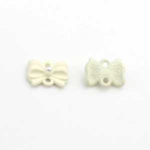 Dettaglio di mini ciondoli a fiocco bianco crema con perle e doppi passanti per il fai da te