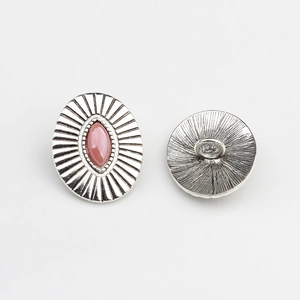Macro detail of vintage silver oval button with pink stone and sunburst pattern