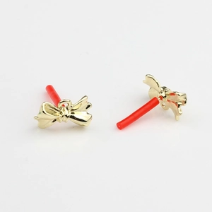 Close-up of golden bow-shaped stud earrings with red protective needle caps