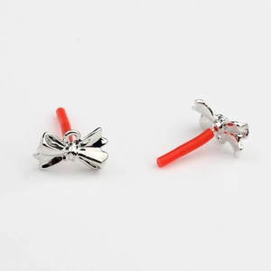 Macro detail of silver bow-shaped jewelry components with protective red ear pin covers