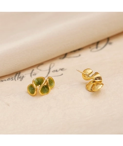 Vue macro de boucles d'oreilles dorées ondulées avec émail vert foncé sur soie
