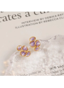 Gros plan de boucles d'oreilles ondulées dorées en émail violet sur un magazine