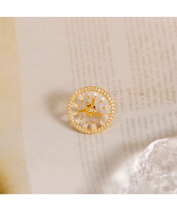 Macro detail of gold clock-inspired brooch with micro-pave crystals on vintage paper