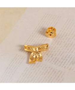 Close-up of golden bow-shaped brooch showing polished metal texture and scarf buckle detail