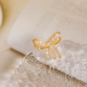 Elegant gold bow brooch set with sparkling cubic zirconia on a glass decorative stand