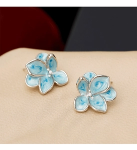 Detailed close-up of light blue enamel flower earrings with marble texture on golden satin