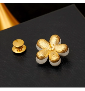 Détail macro d'une broche marguerite avec pétales dorés et perle sur fond noir texturé
