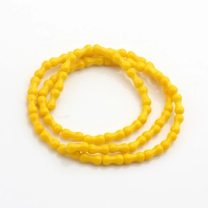 Dettaglio di perline di vetro giallo brillante a forma di osso per gioielli fai-da-te
