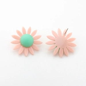 Gros plan de boucles d'oreilles marguerites en résine rose avec cœur vert et tige en métal