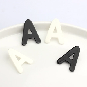 Minimalist black and white acrylic letter A stud earrings displayed on white ceramic tray