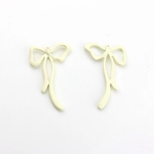 Close-up of cream white bow pendants with metal alloy texture for DIY jewelry making
